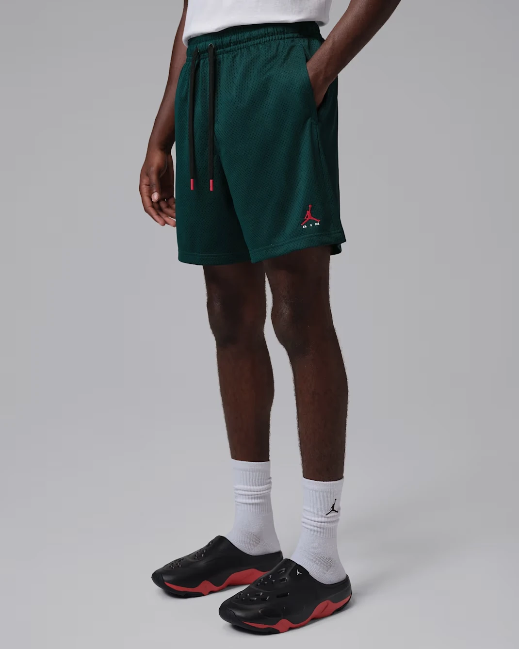 Model wearing Jordan Brooklyn mesh shorts in Midnight Spruce with University Red accents.