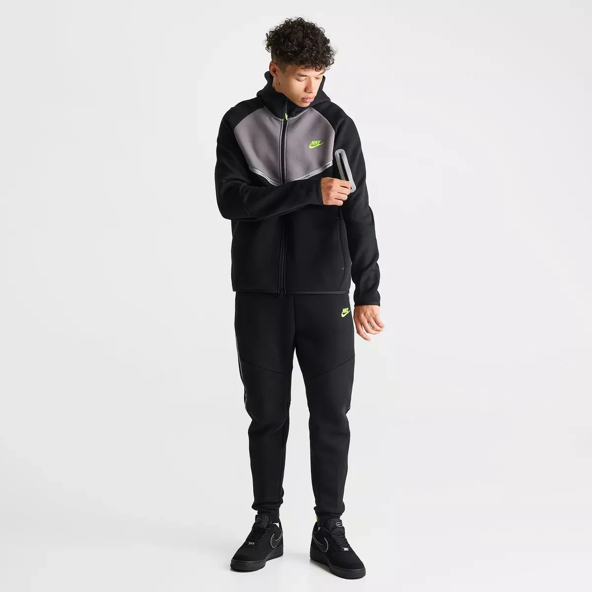 Model wearing the Nike Tech Fleece Reflective Windrunner Hoodie and matching black joggers with Volt accents and Nike Air Force 1 sneakers.